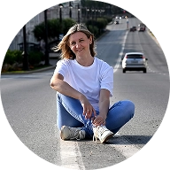 A woman sitting on the road, with a city skyline visible in the background.